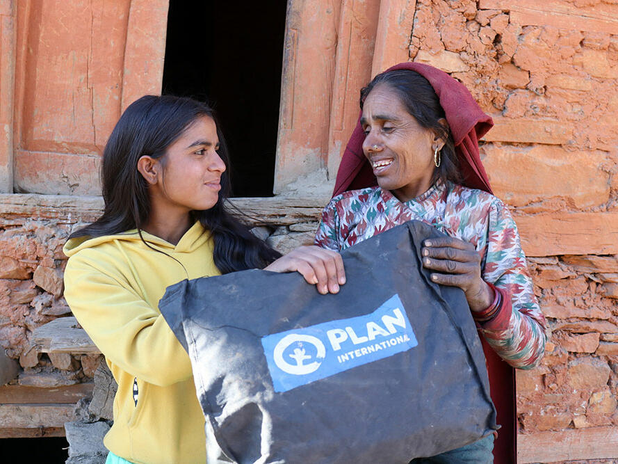 Sarita and her mother standing outside their home holding a Plan dignity kit