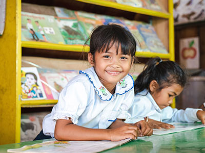 Vorn, 7, reads a book in the library at primary school built by Plan International in Cambodia