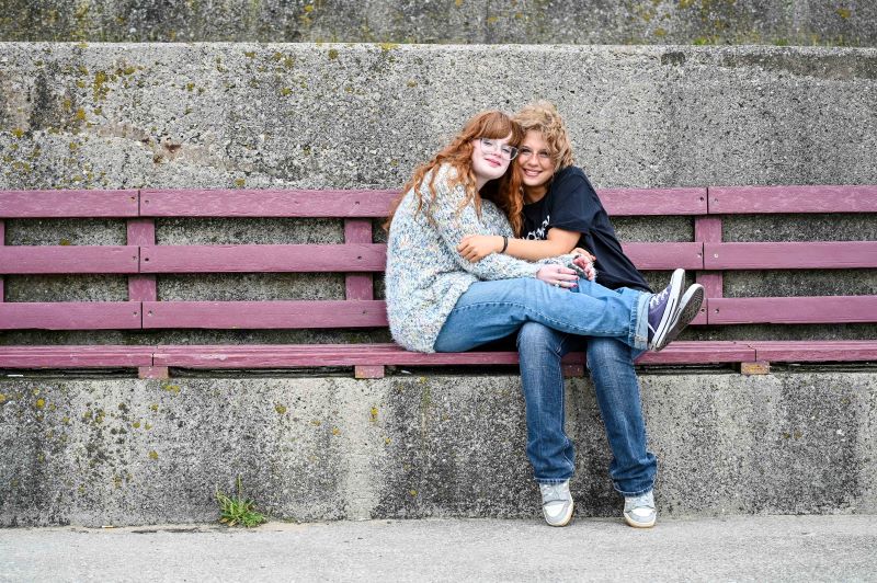Two girls sat on a bench smile at the camera
