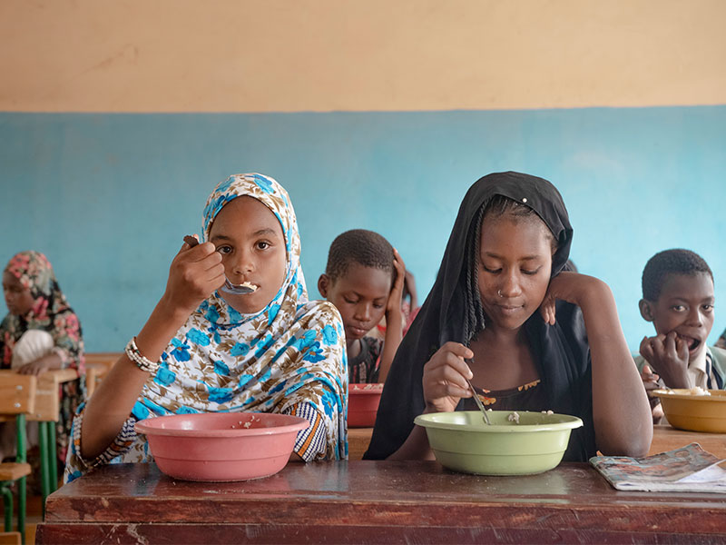 Children eating lunch in school classroom, with 2 girls in forefront.