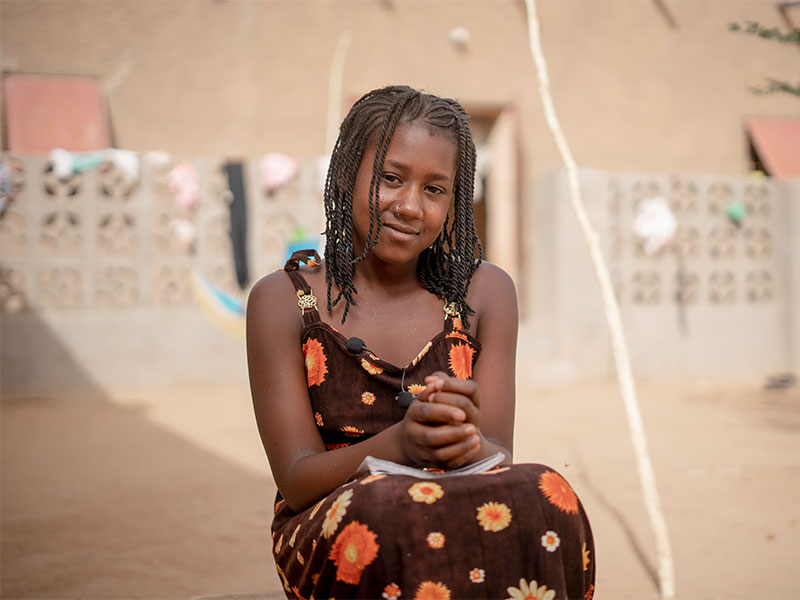 Aminata sitting outside with hands on lap smiling at camera.