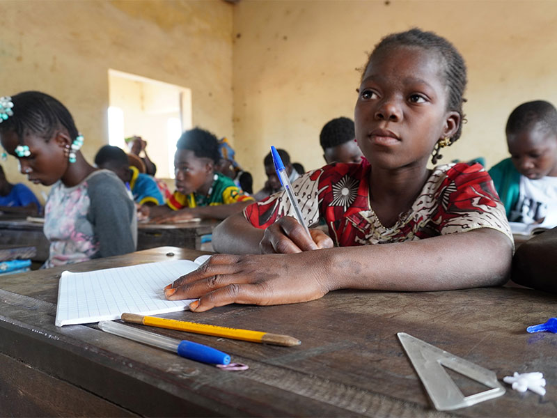 Diatou, learning in class at her school with more pupils writing notes in the background.