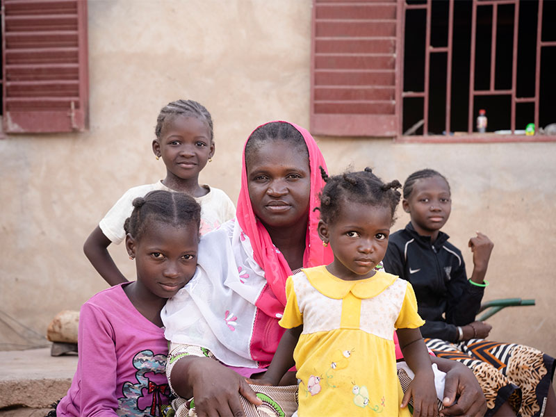 Moussou sitting next to her mom and 3 siblings outside their home. All looking at camera.