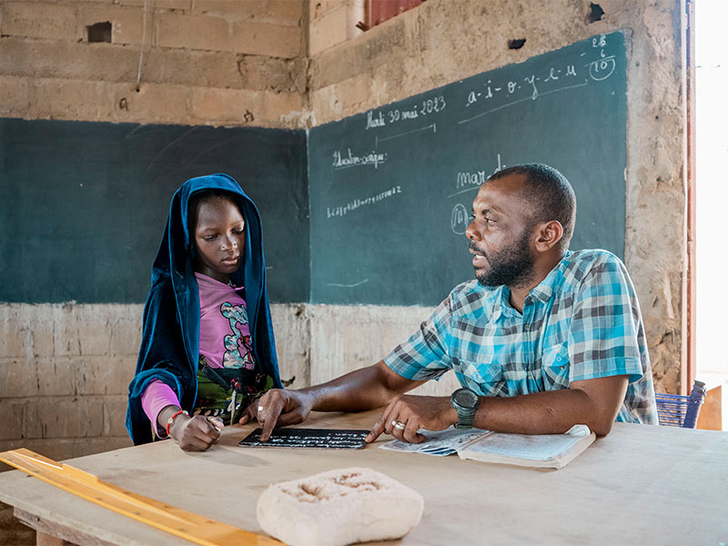 Moussou being helped with schoolwork by teacher in classroom.