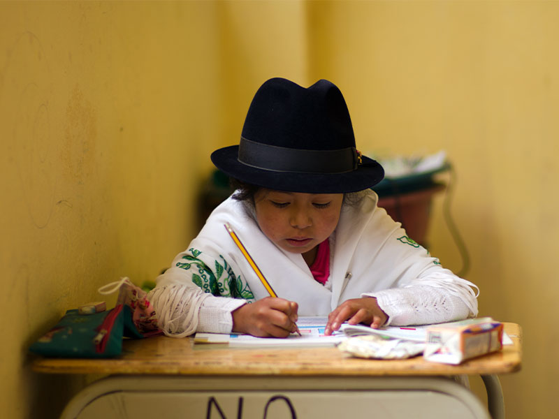 Anahi writing in book at school desk. 