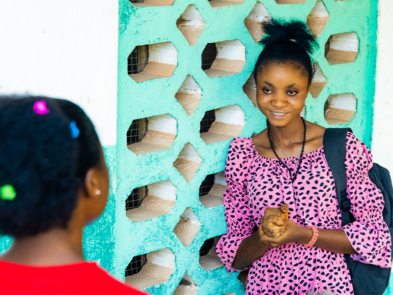 Eunice standing in front of teacher training centre speaking to somebody. 