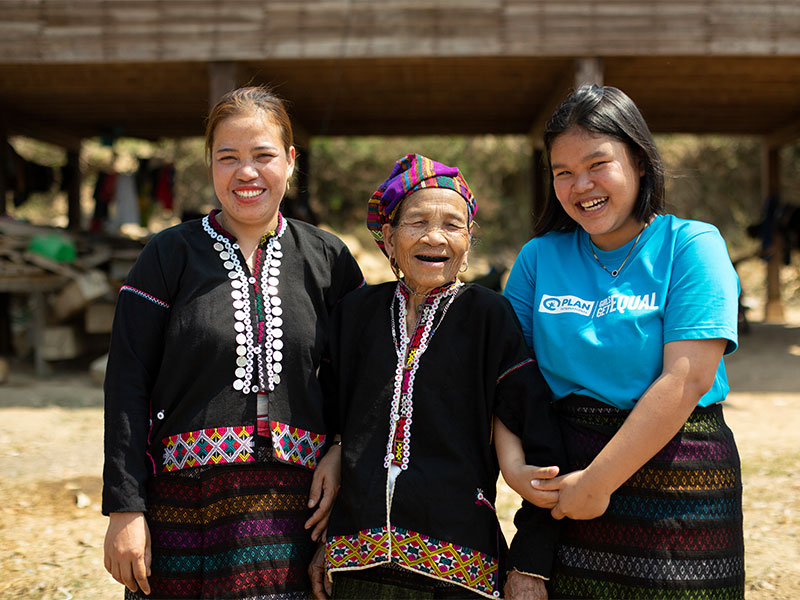 Grandmother standing outside with her daughter and grandaughter, all smiling and linking arms