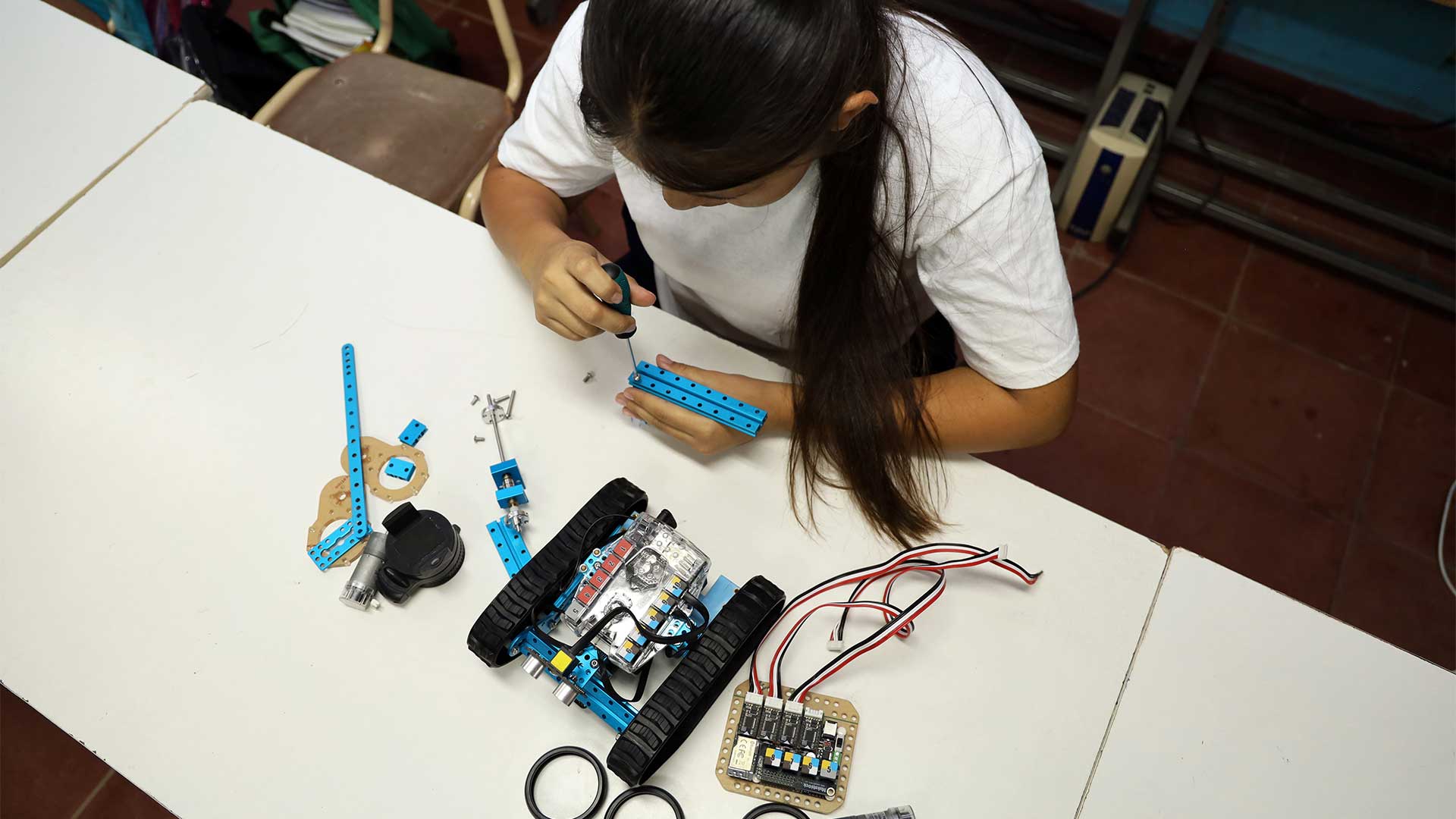 Birds-eye view of top of girl working with electrical equipment laid out on table.