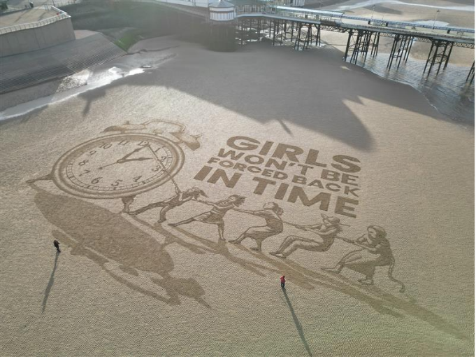 Sand art of a clock face with girls pulling the clock hands and the words 'Girls won' be forced back in time'