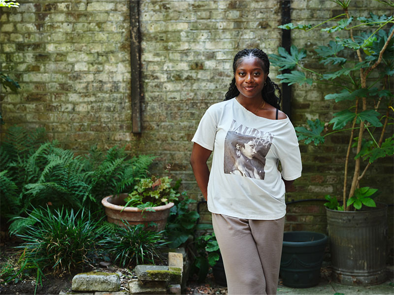 Headshot of Edwina standing outside with brick wall and plants in background
