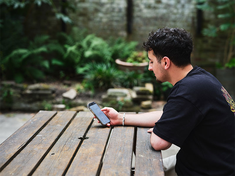 Ilyas sitting at bench outside reading something on his phone