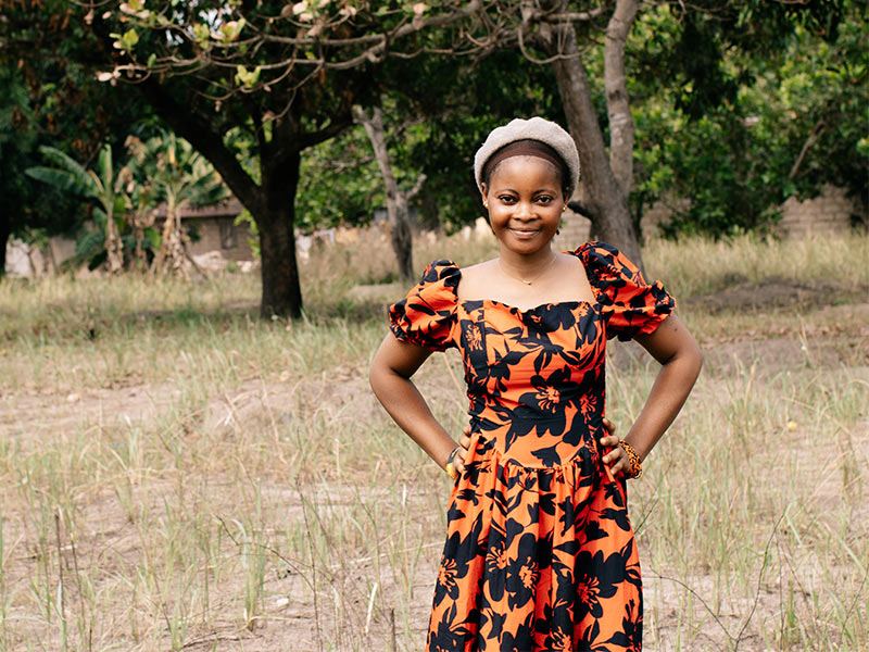 Fatmata standing outside with hands on hips, and grass and trees in background