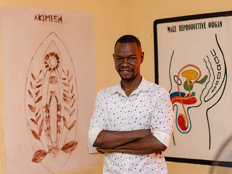 Ibrahim standing in centre with diagrams of reproductive systems on walls behind him