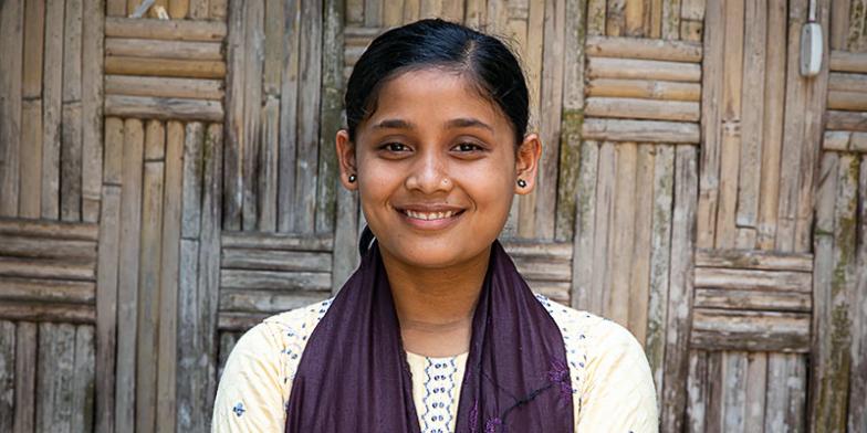 Girl standing in front a wooden wall, smiling at the camera.