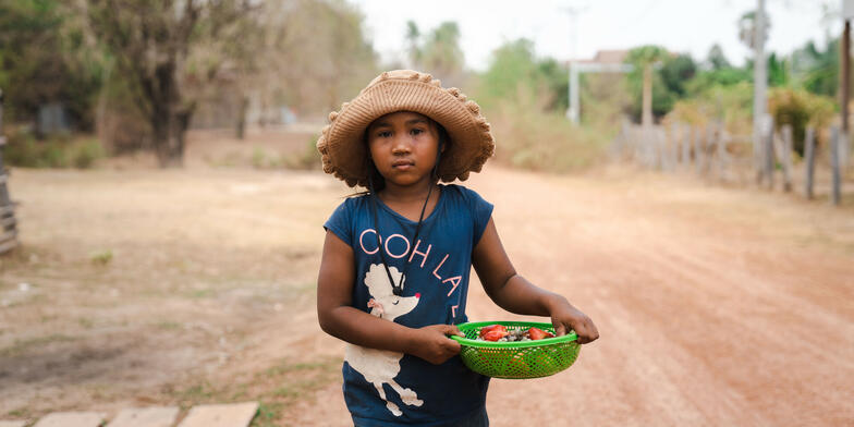 Len Sokha, 10, carrying a bowl of vegetables on a dirt road in Cambodia