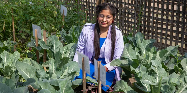 Akhimoni, 15, sitting amongst the plants in her family's vegetable garden in Bangladesh