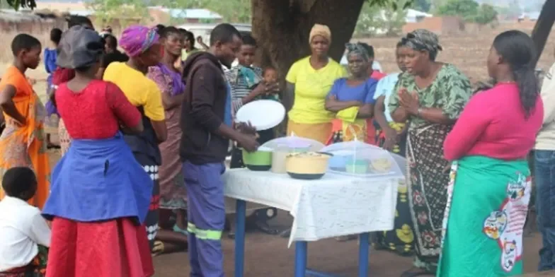 Group of people standing around a table of food cooked during a cooking demonstration.
