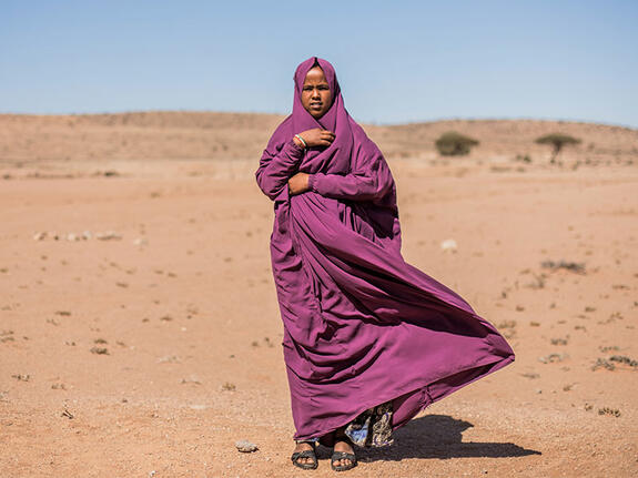 Hamda standing outside in sandy landscape wearing purple robes/headscarf