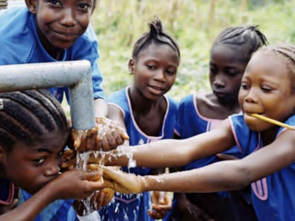 A group of children get water from a stand pump in a village in Africa