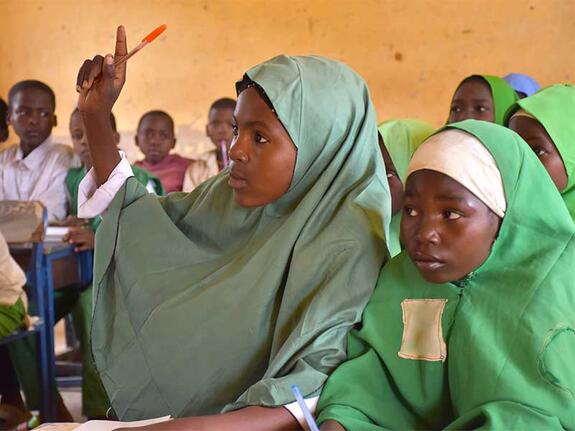 Aisha in classroom with her hand held up and other students around her.