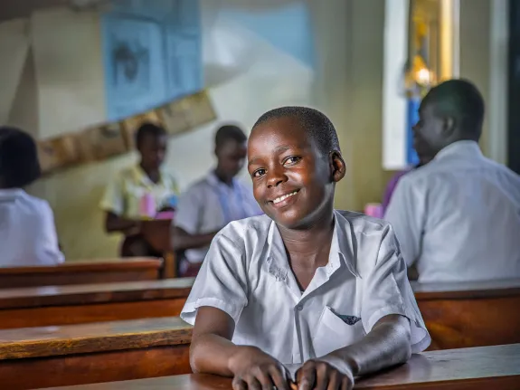 Melisa sitting at school desk smiling at camera with other students out of focus in background