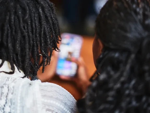 Two members of YAP sit side by side, scrolling on a mobile phone.