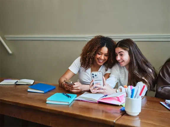 Dania and Elaf looking and smiling at something on Ealaf's phone. 