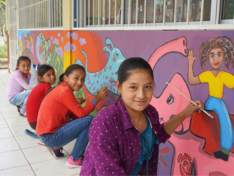Ana, 17, paints mural with her drawing club in community school