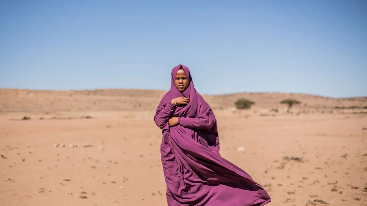 Hamda standing outside in sandy landscape wearing purple robes/headscarf