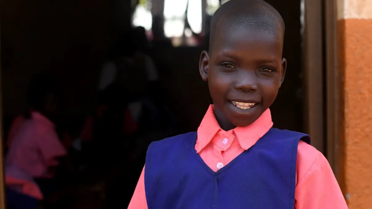 Immaculate, 10, standing outside her school in Uganda smiling at the camera