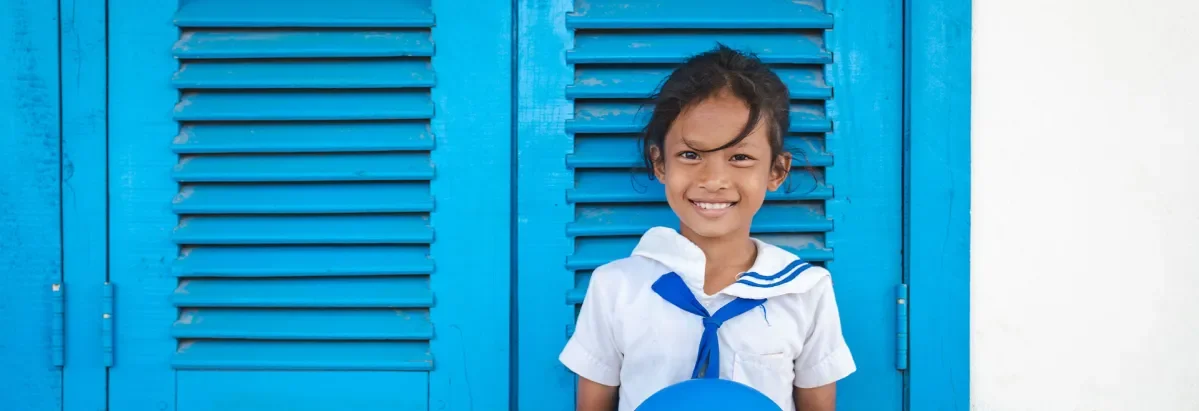 Phen, standing in front of blue shutters in school uniform smiling at camera