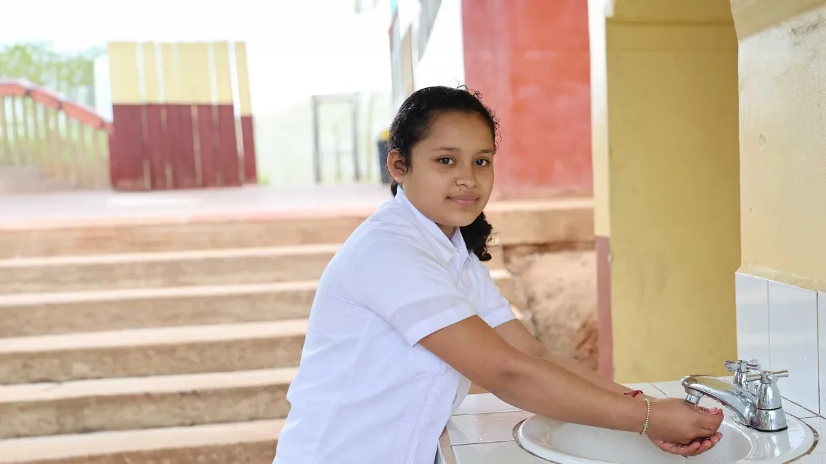 A girl washes her hands and looks at the camera