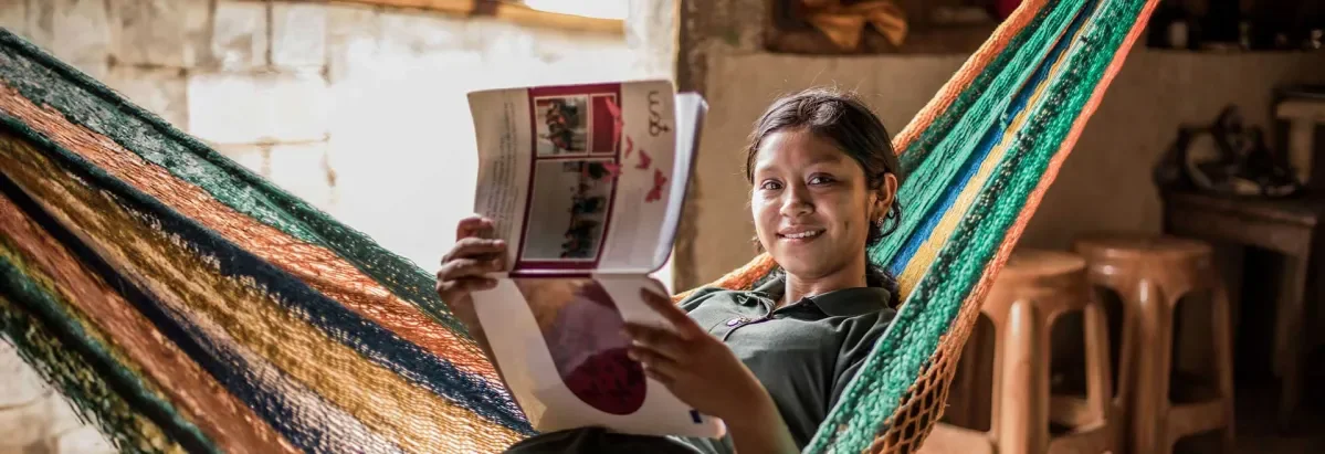 Ana, sitting in a hammock holding exercise book about developing advocacy skills and smiling at camera.