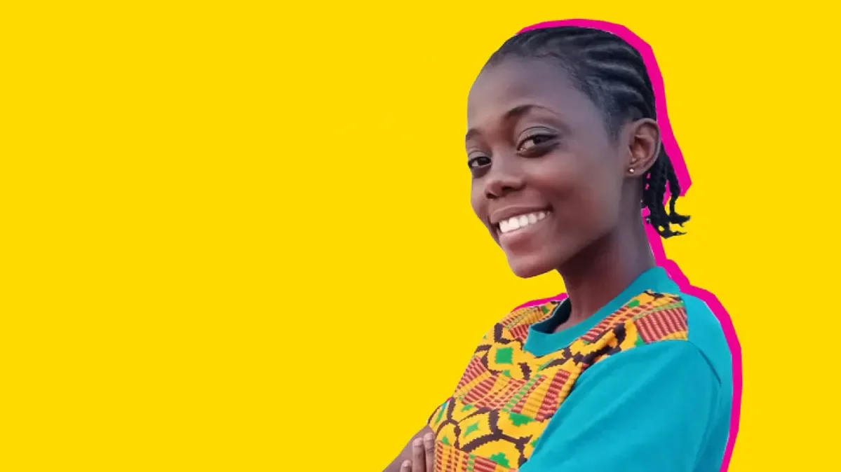 A girl standing against a yellow background smiling at the camera.
