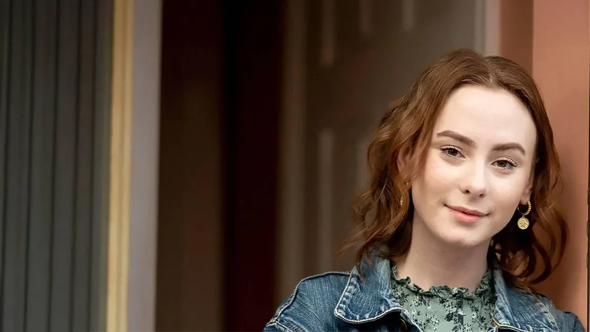 A teenage girl with red hair looking straight at the camera with slight smile