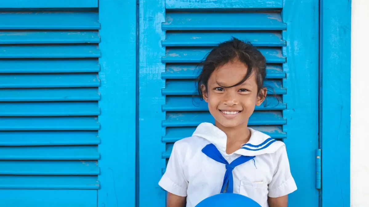 A girl standing against a blue wall in her school uniform.