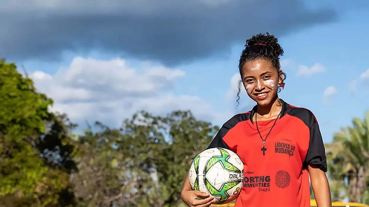A girl wearing a Sporting Communities t-shirt holding a football