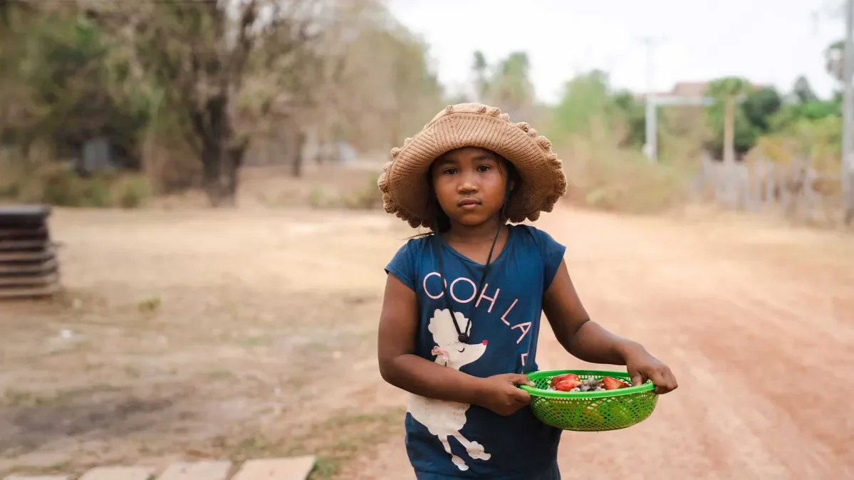 Len Sokha standing outside holding a basket of fruit and a sunhat on
