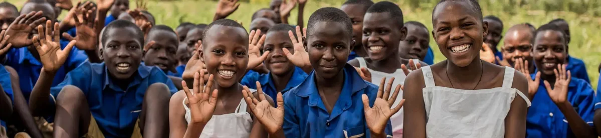 A group of African school children smiling and waving at the camera