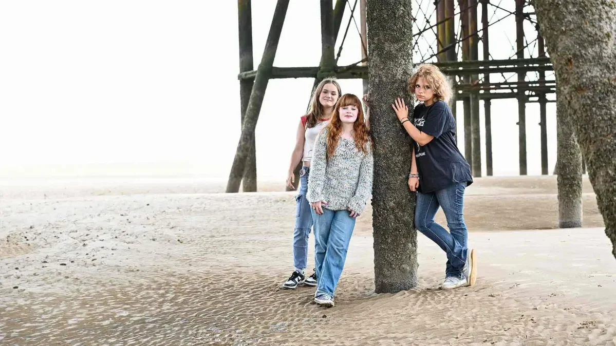 Three teenage girls stand on a beach in Blackpool.