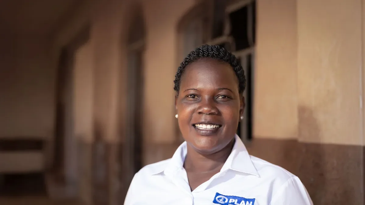 Plan International staff member standing in front of building in Plan International branded polo shirt.
