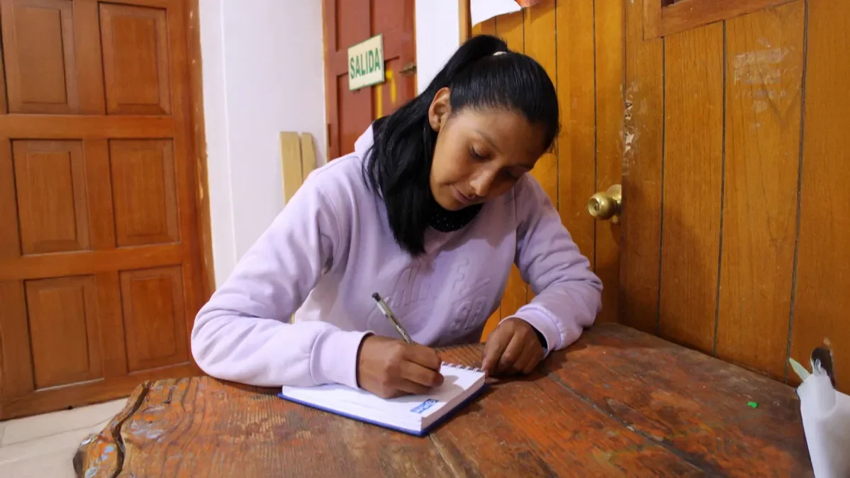 Sonia sat at desk writing in notebook.