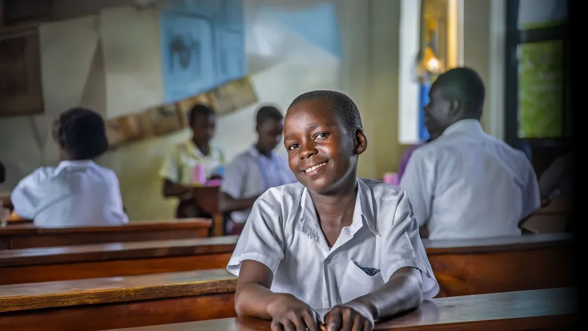 Melisha sitting at school desk smiling at camera with other students out of focus in background
