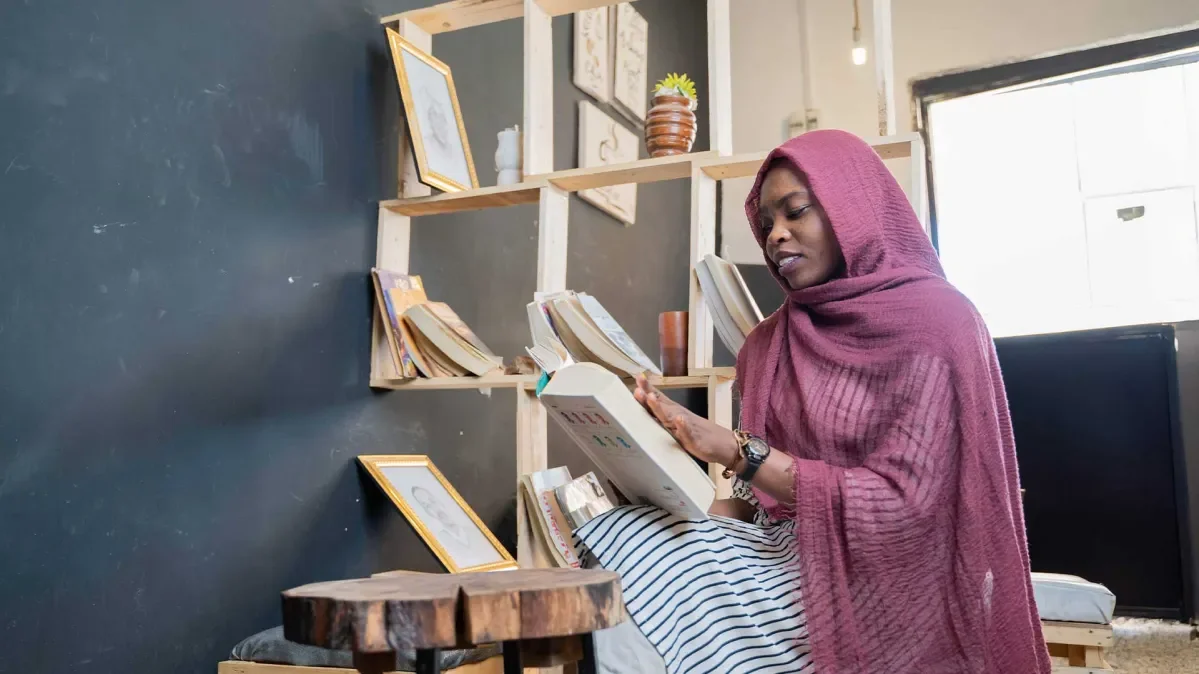 Safa sat down reading in her cafe. There is a shelf of books behind her.