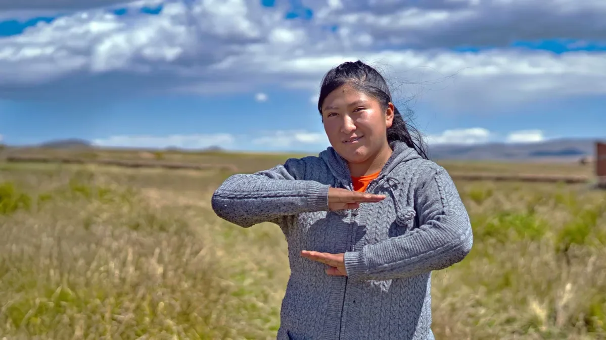 Geovana standing in field with arms out in front of her gesturing no to patriarchy