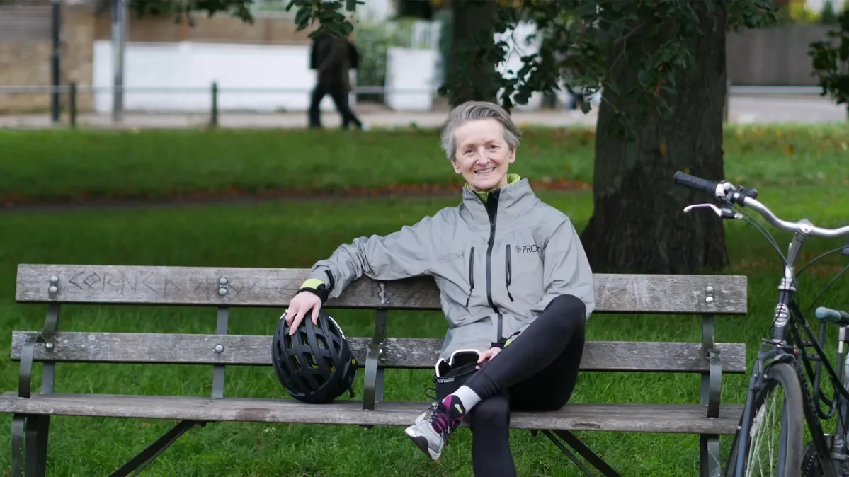 Francesca sat on park bench with bike helmet in hand and bike parked next to her.