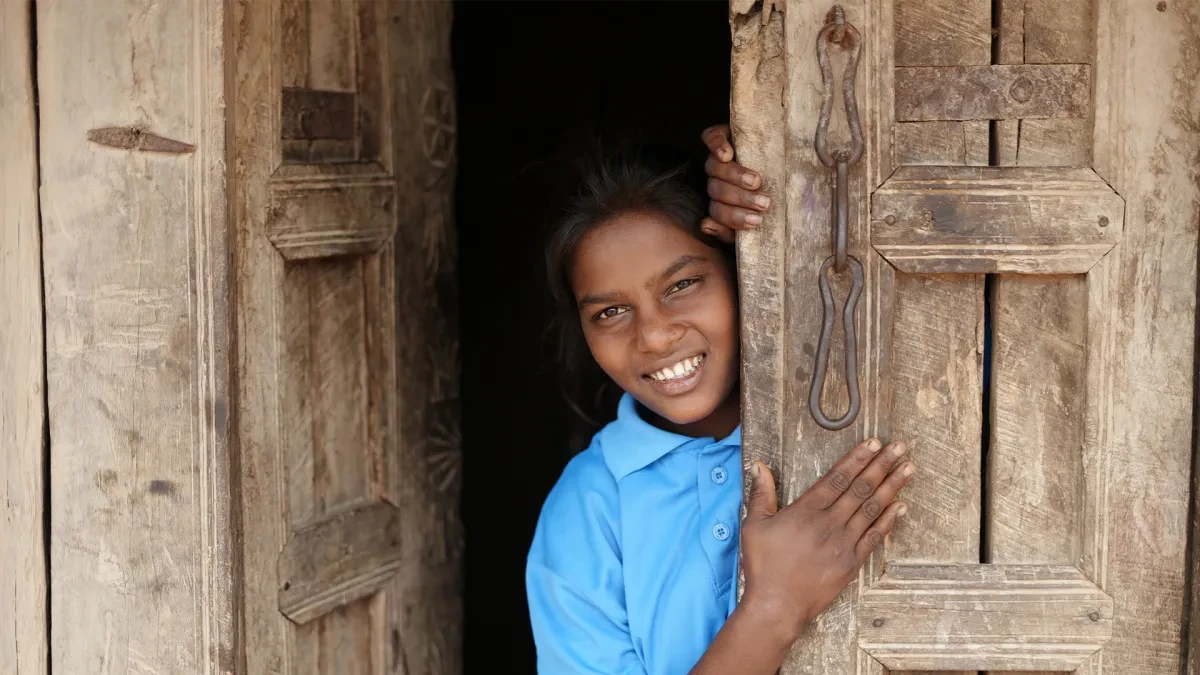 Rajni standing in doorway looking out and smiling at camera