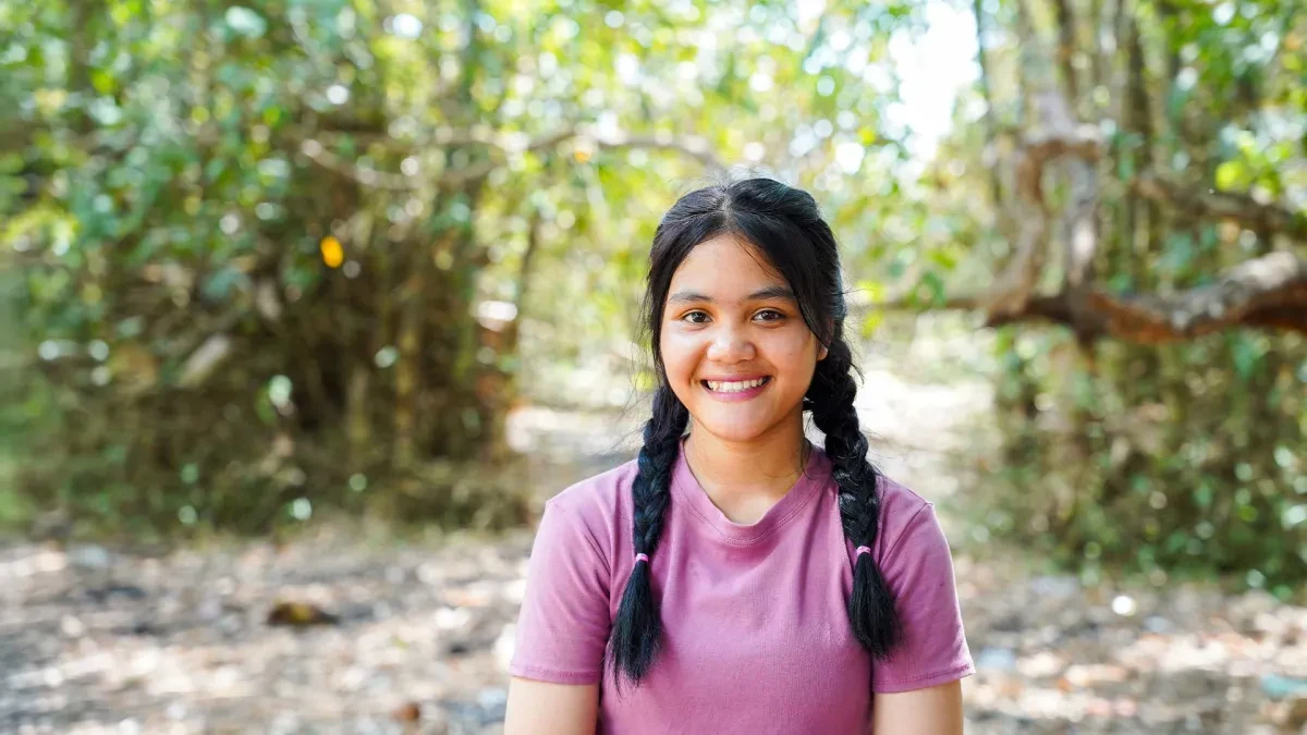 Sopheak standing outside siling at camera with out of focus trees in background
