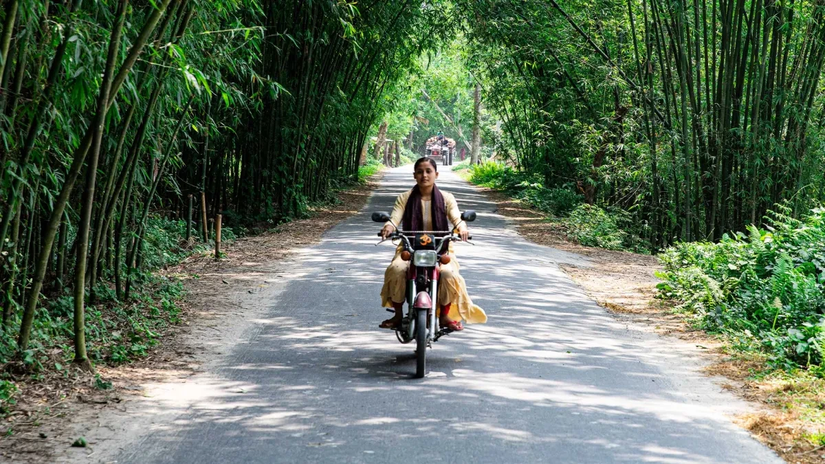 Antora riding her motorbike down a tree-lined road in Bangladesh