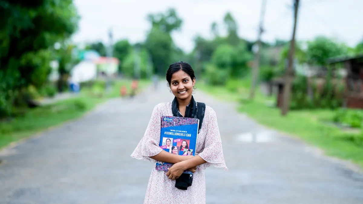18-year-old Rahimat holds a book in her arms as she smiles at the camera.